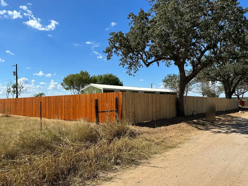 Cedar privacy fence along a dirt road, half stained.
