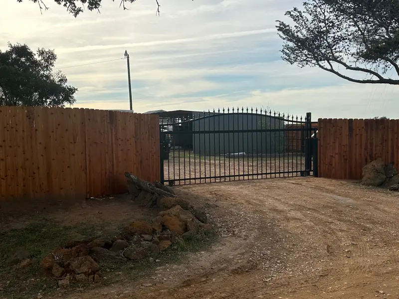 Black steel arched drive gate between stained cedar fence sections.