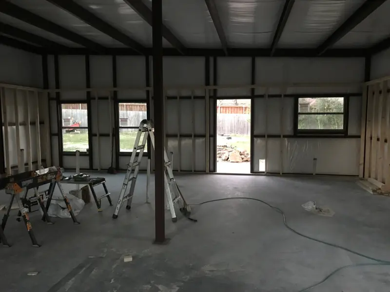 Open interior of a metal building with windows and a door in place and wall framing started.