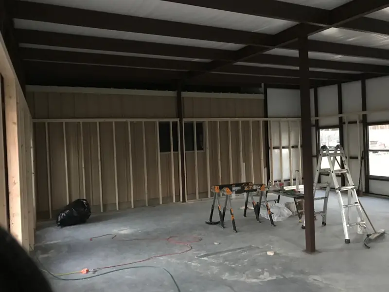 Wood wall framing going up along the steel wall of the building, sawhorses on the slab.