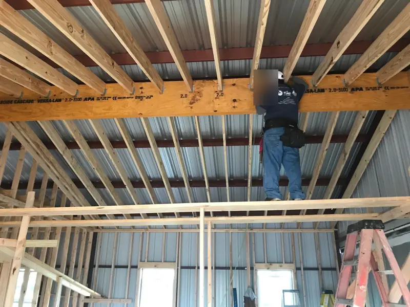 Worker in a hard hat on scaffolding fastening joists to an engineered wood beam.
