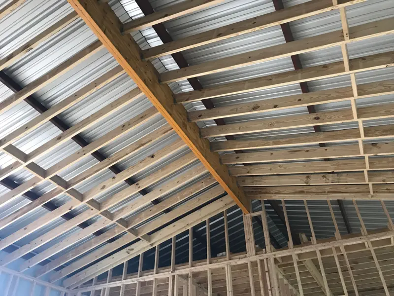 Wood rafters and a ridge beam framed under the steel building's roof.