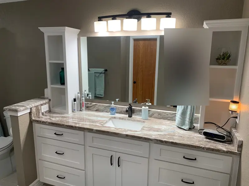 Bathroom vanity with white tower cabinets, a marble-look top and a long mirror.