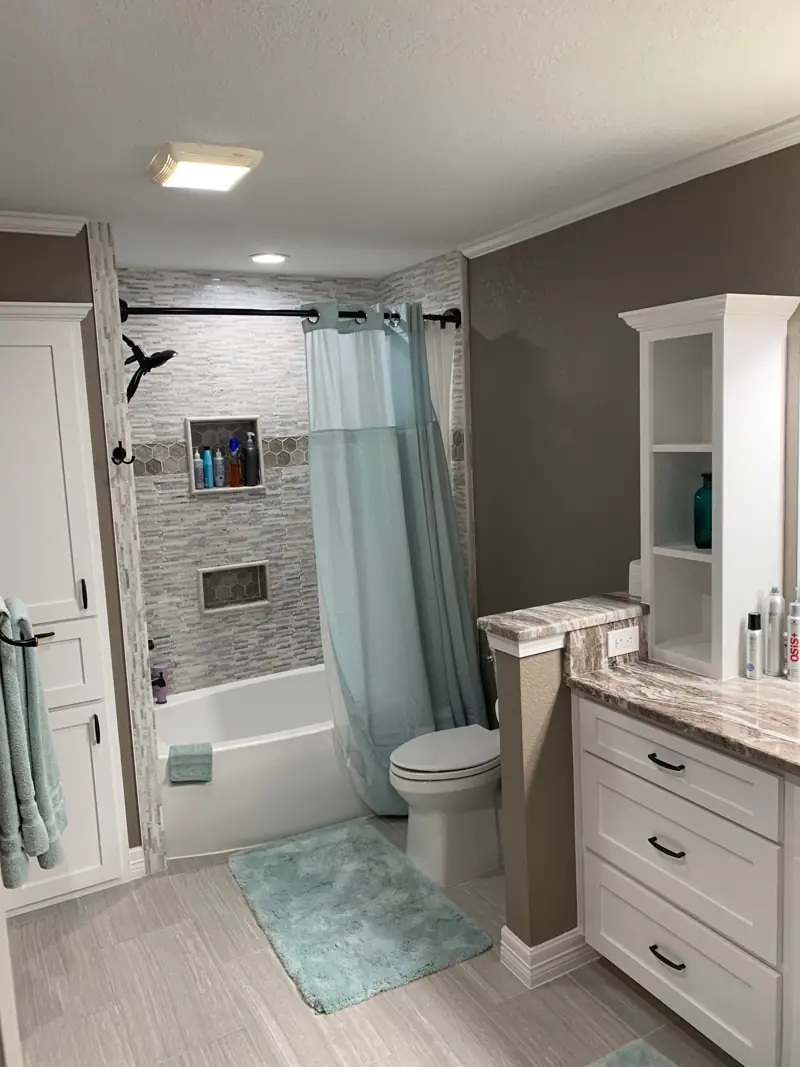 Tub with a tile surround, a mosaic stripe and niches, beside a white vanity tower.