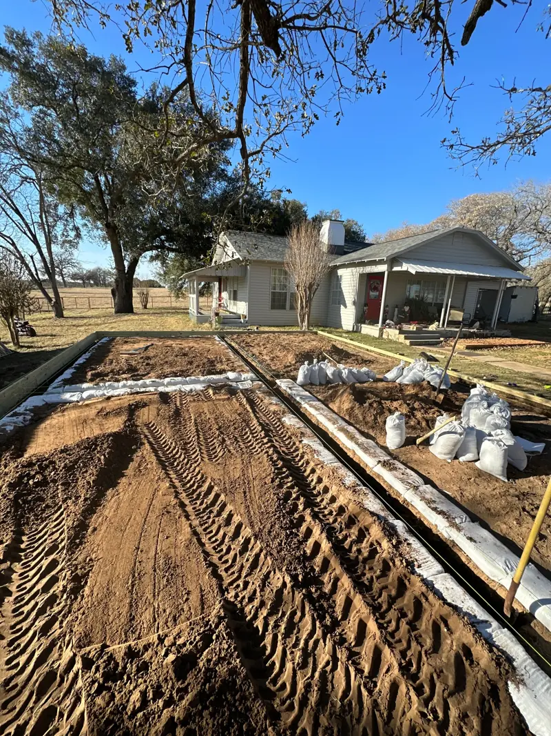 Leveled dirt pad inside wood forms, with sandbags along the edges and the house beyond.