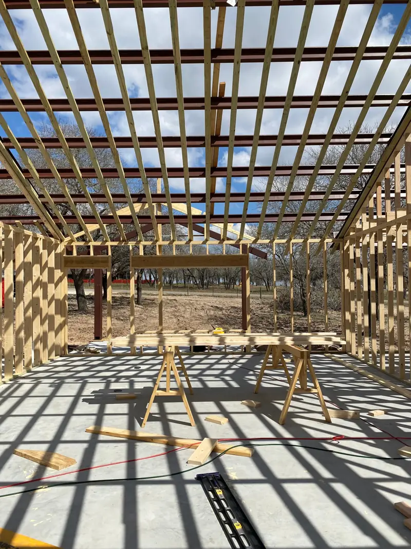 Wood walls framed under open roof purlins, sawhorses on the slab.