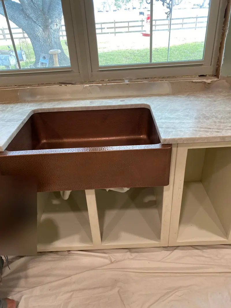 Copper farmhouse sink set in a new counter under a window.
