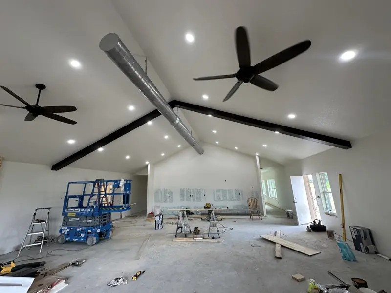 Vaulted ceiling with dark false beams, recessed lights and two ceiling fans, a scissor lift below.
