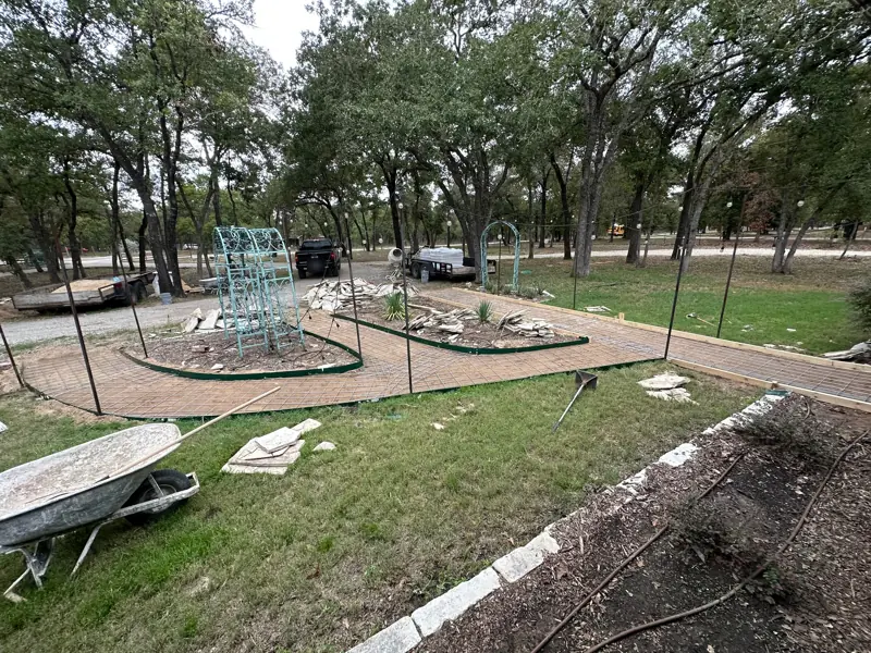 Forms and rebar along curved garden beds with metal arbors, flagstone stacked on the grass and a wheelbarrow nearby.