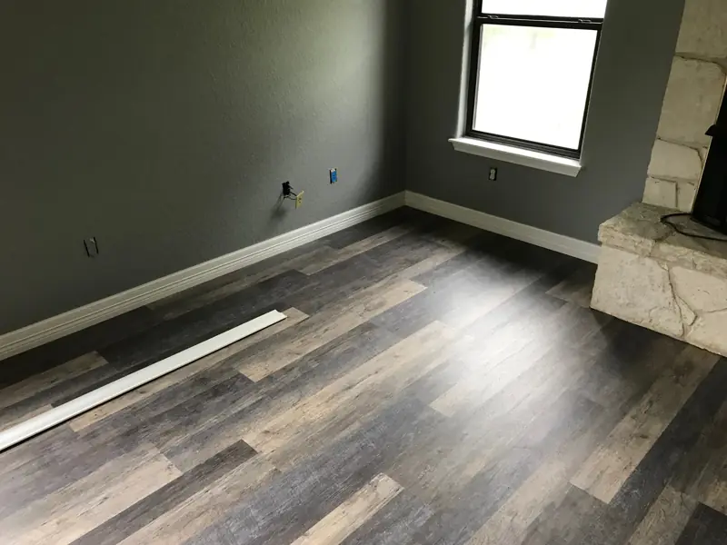 Living room with a new wood-look plank floor, gray walls and white baseboards by a stone hearth.
