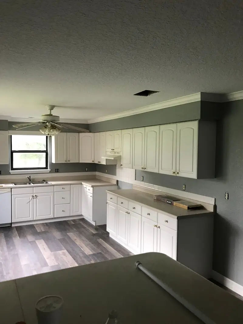 White kitchen with the new plank floor and gray walls.