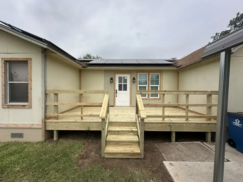 New treated wood deck with railings and steps at the door of the remodeled house.