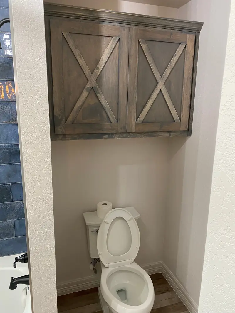 Custom wood cabinet with X-pattern doors over the toilet.