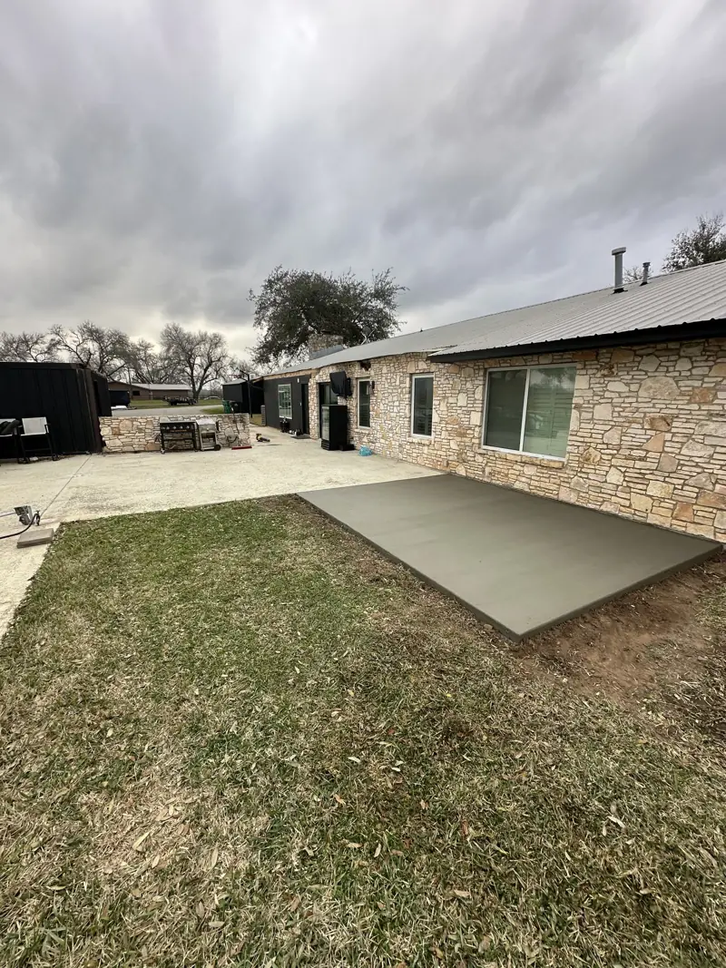 Fresh concrete slab poured against the stone house wall on the lawn for a new covered patio section.