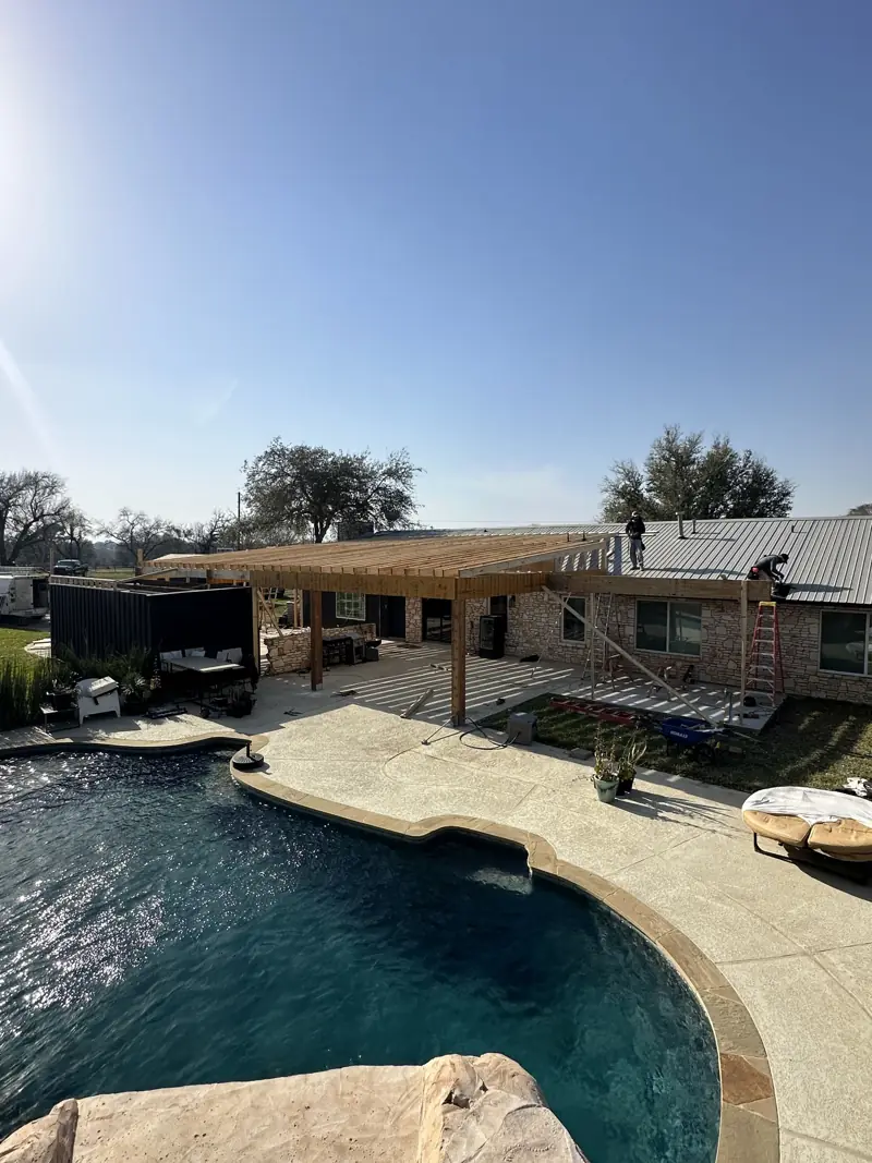 Crew on the house roof tying in new wood patio framing, seen from above the pool.