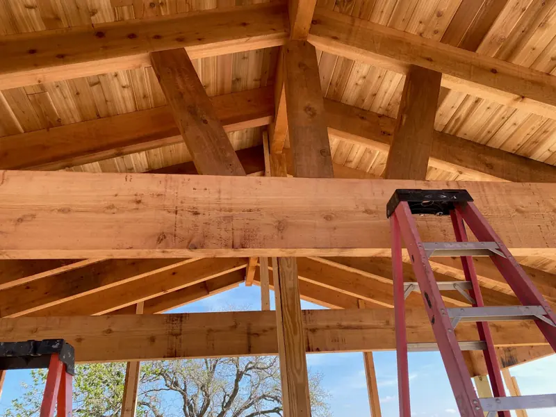 Close view of a cedar beam and rafters, a ladder below.