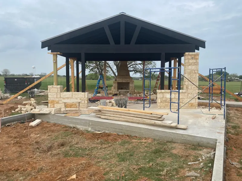 Pavilion with black beams, stone columns, and the fireplace and chimney at the back.