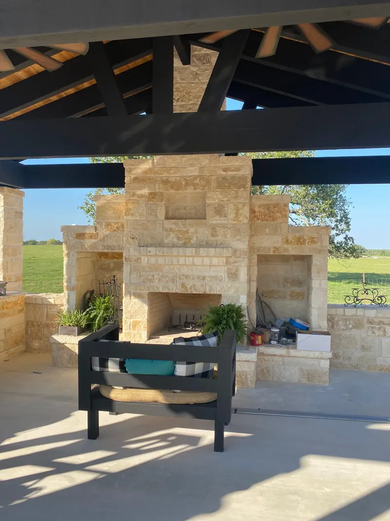 Finished stone fireplace and chimney under the pavilion, with seating in front.