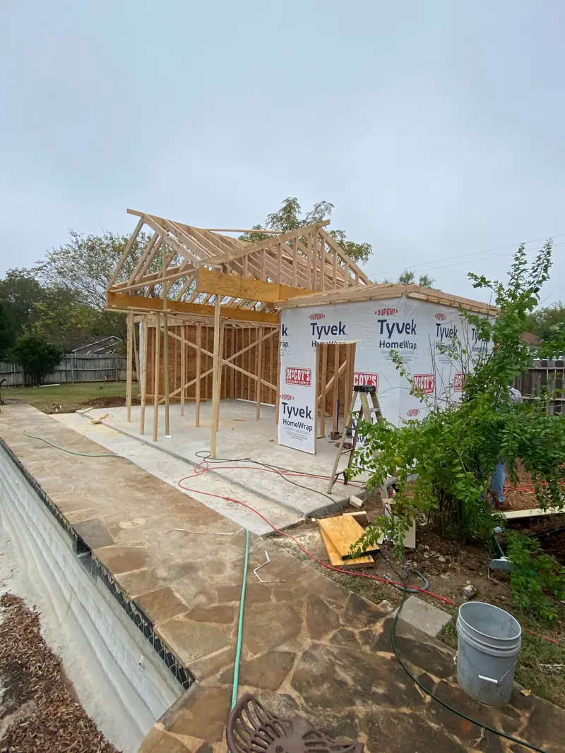 Pool house framing in house wrap beside a flagstone patio.