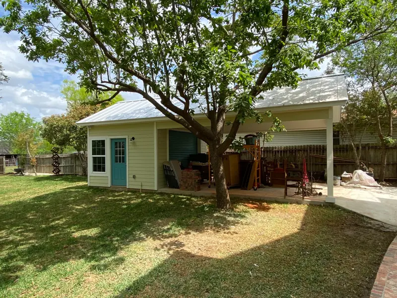 The yard with the carport and a small building with a teal door.