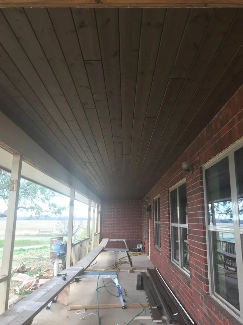 Wood tongue-and-groove ceiling going up along a long porch on a brick house.