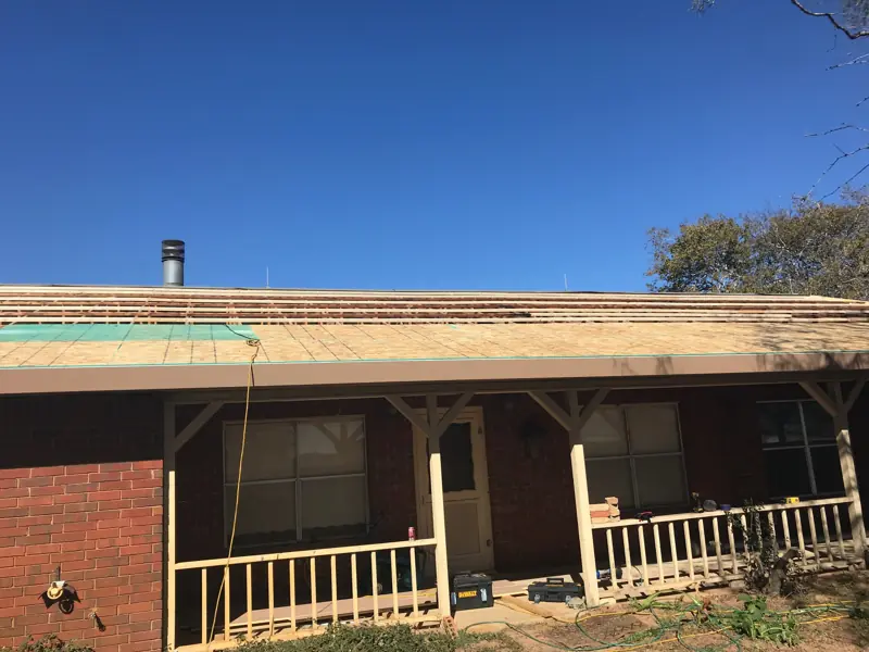 Brick ranch house with a front porch, new roof decking going on over the old roof.