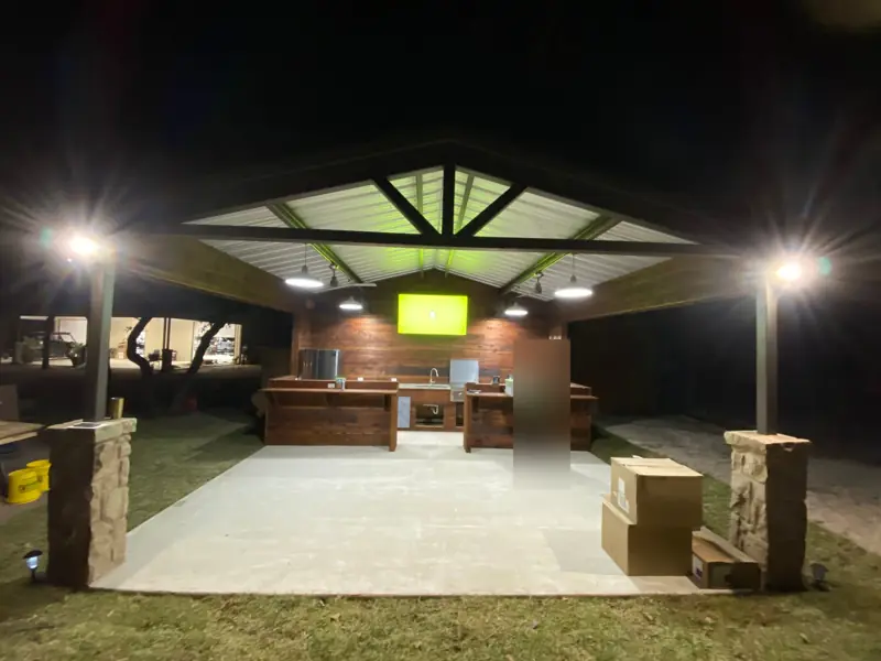 Finished pavilion lit at night, with the outdoor kitchen and stone column bases.