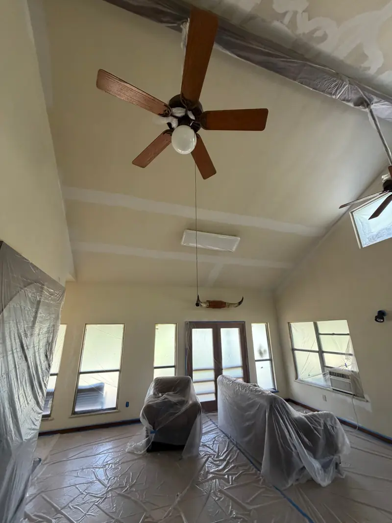 Living room with a freshly painted vaulted ceiling, furniture covered in plastic.