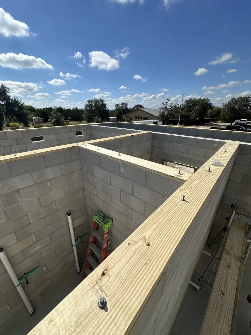 Treated wood plates anchored on top of concrete block walls, with plumbing stubs and a ladder inside.