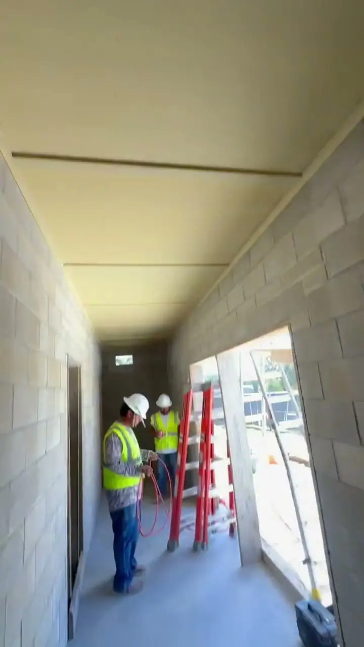 Inside the new concrete block building: a hallway with block walls, a panel ceiling and two crew members in safety vests.