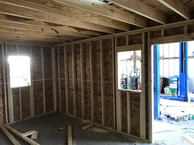 Inside the new office with sheathed stud walls, a window looking out to a car lift.
