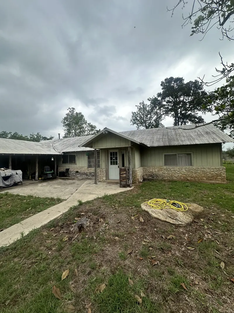 House before the work: pale green siding, a stone skirt and a front porch.