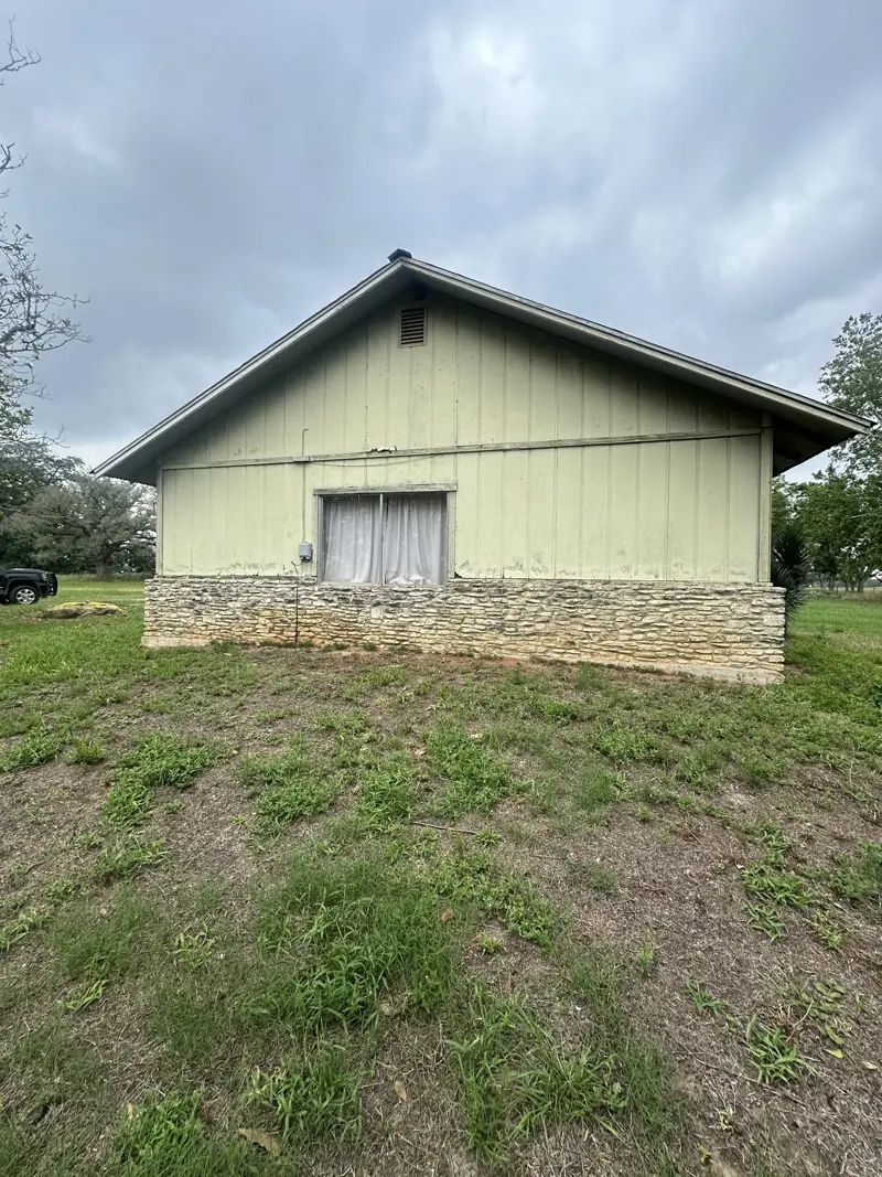 Gable end before the work: pale green siding over a stone base.