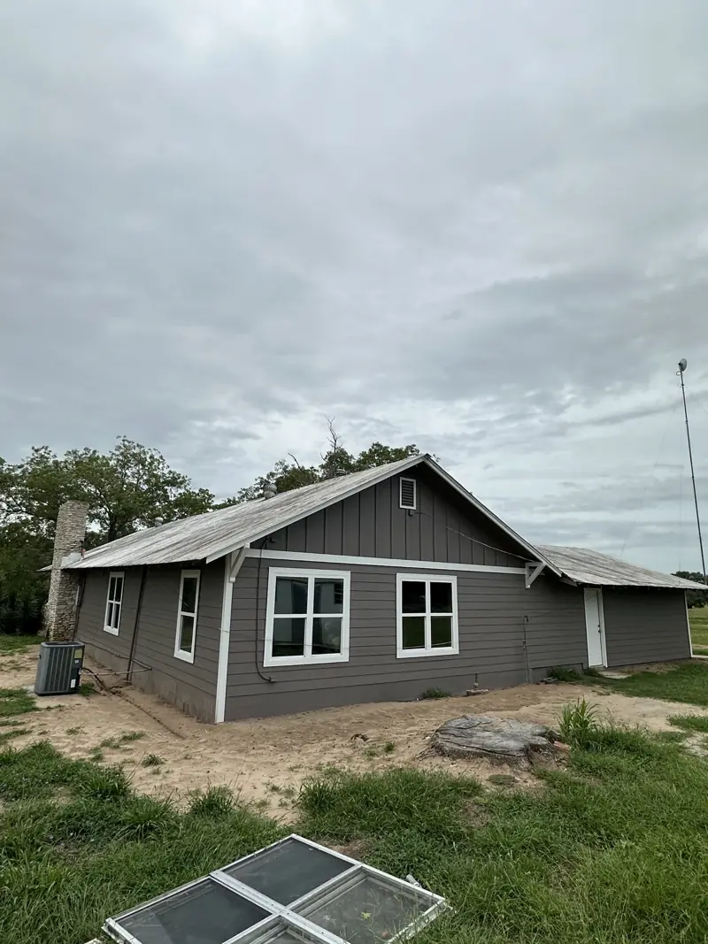 The house after: gray siding, white trim and new white windows, with the old windows on the ground.