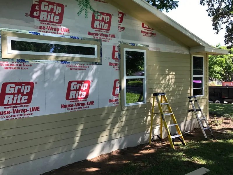 House wrap on the wall, a new wide window up high and tan lap siding going on below it.