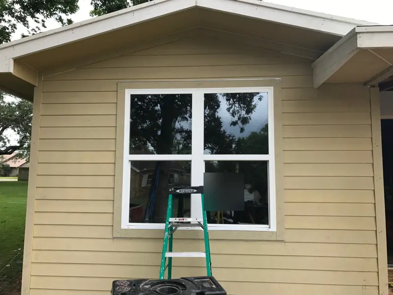 New white double window in the tan lap siding of a gable end.