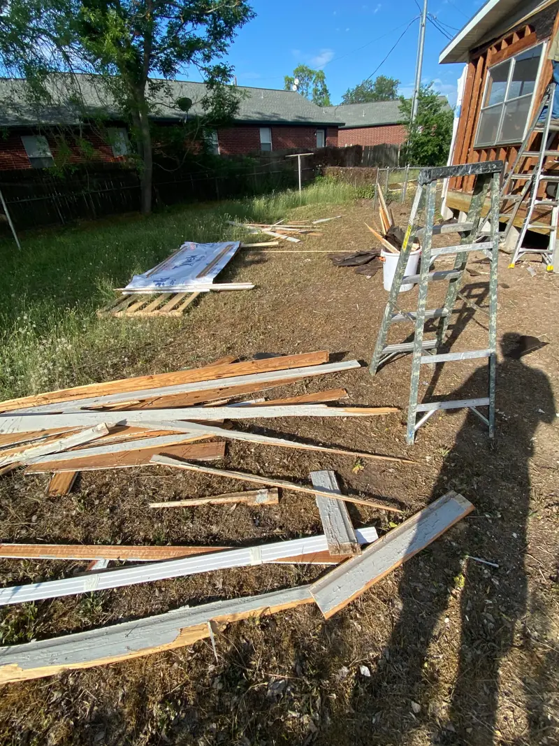 Old siding and boards piled in the yard beside the stripped wall.