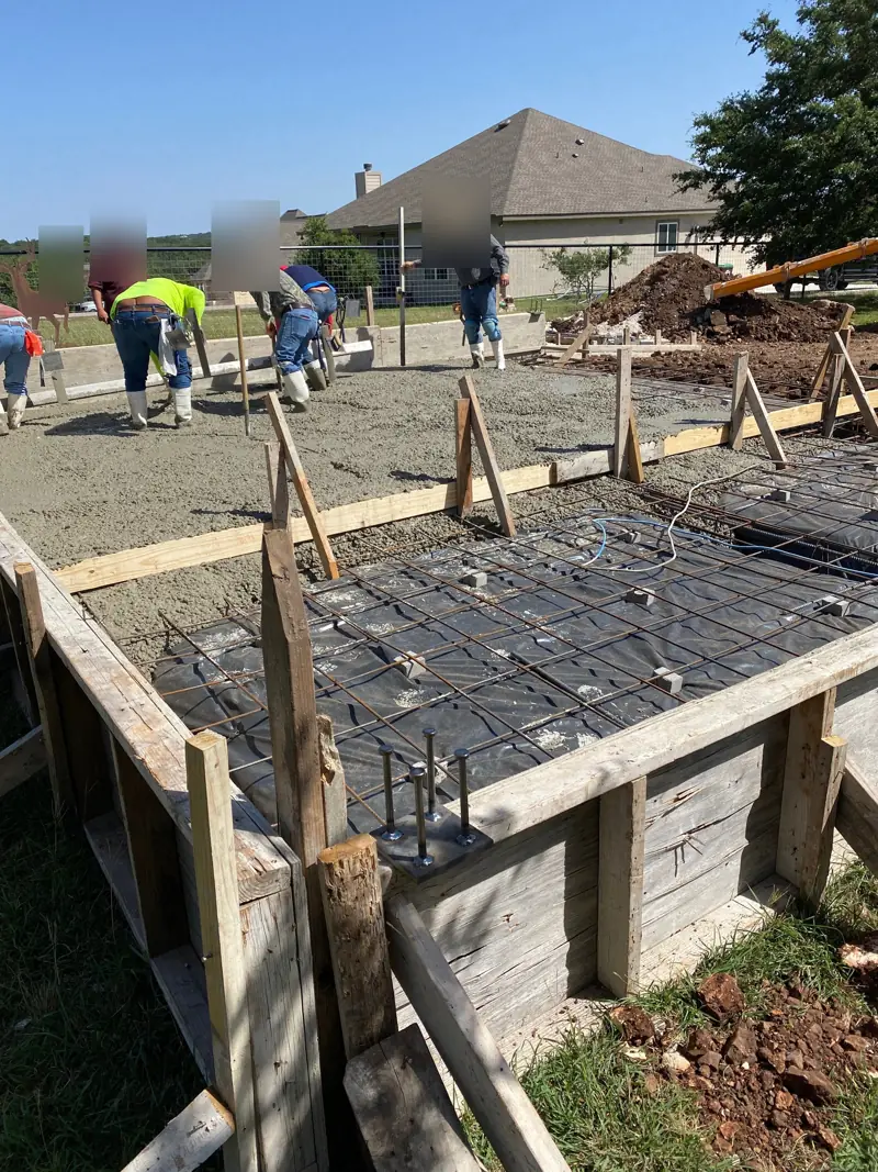 Crew placing concrete over rebar mats inside wood forms.