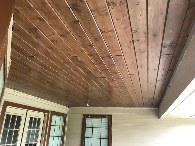 Stained wood porch ceiling over French doors on a house with white siding.