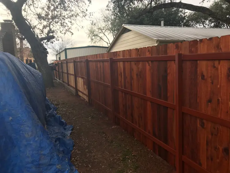 Long run of the stained cedar privacy fence beside a house and a metal building.