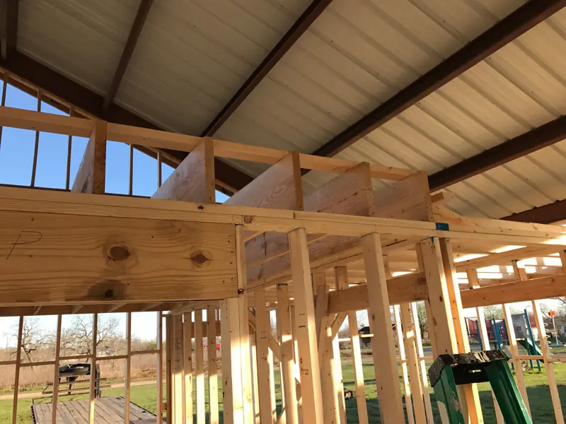 New wood ceiling joists resting on a doubled header over framed walls, under the steel roof.