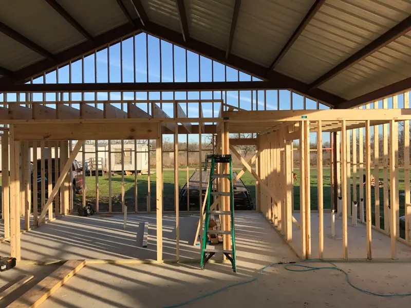Framed rooms and a tall stud gable wall under the steel roof frame, a ladder in a doorway.