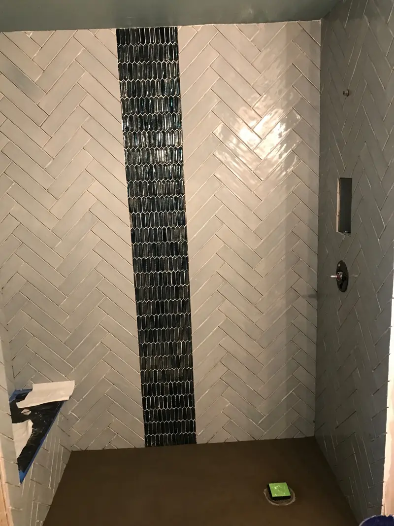 Herringbone white tile on the shower walls, with a vertical stripe of dark blue glass mosaic.