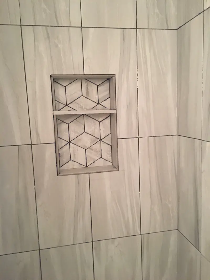 Tiled niche with a geometric marble mosaic and a shelf, set in gray plank tile.