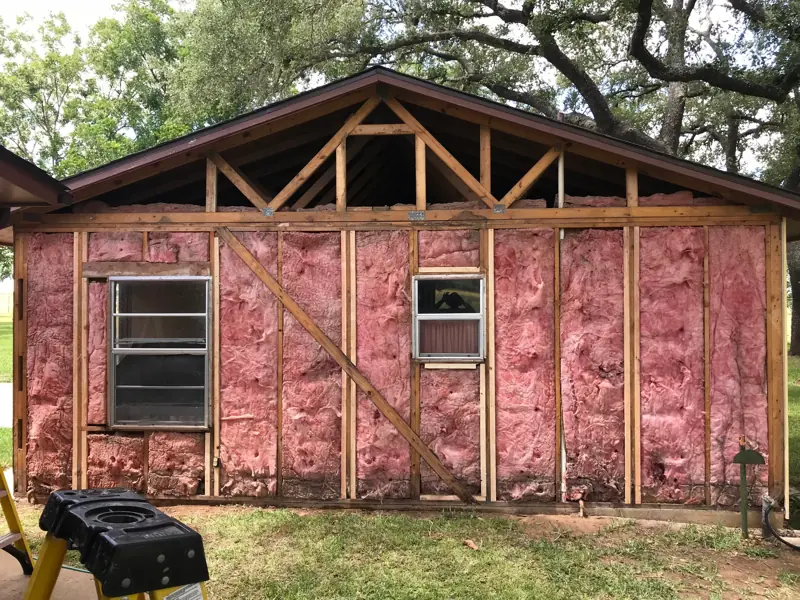 Gable end stripped to the studs and pink insulation, with the roof framing open above.