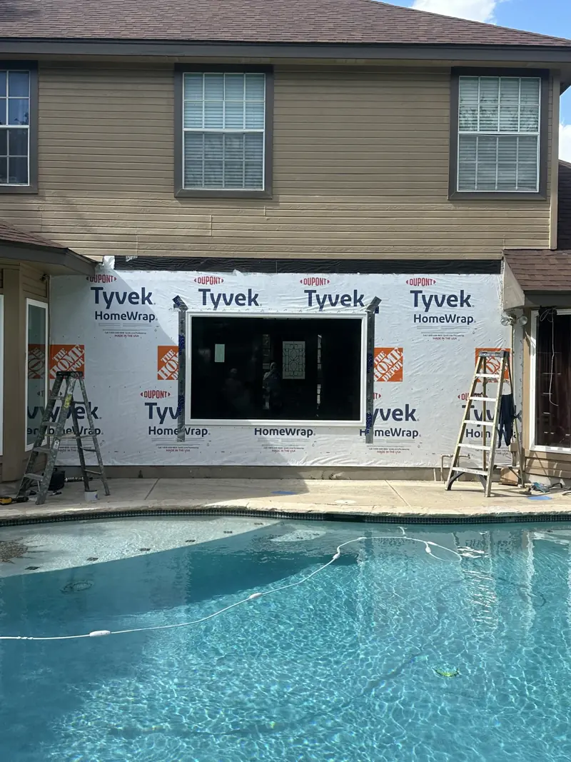 Outside wall in house wrap with the new window set and flashed, seen from across the pool.