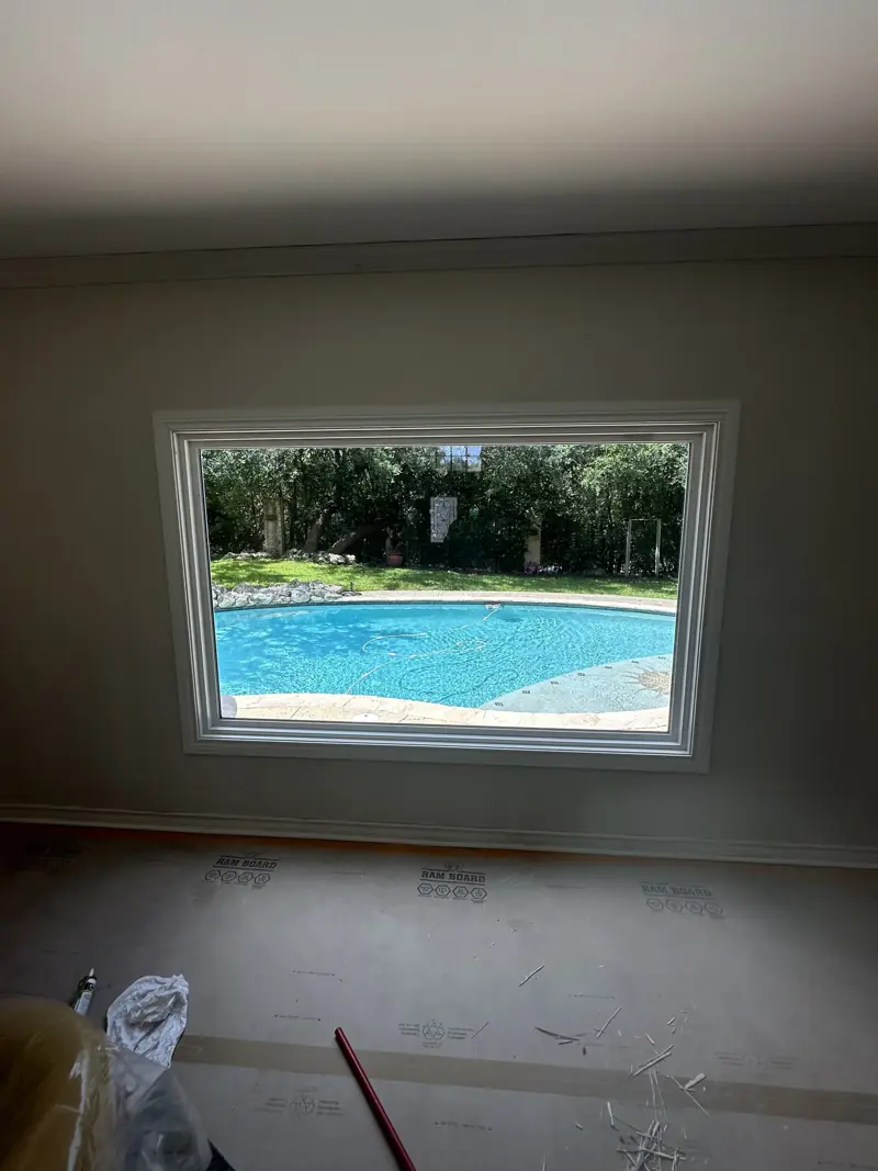Finished window with white casing on a painted wall, looking out at the pool, floor still covered.